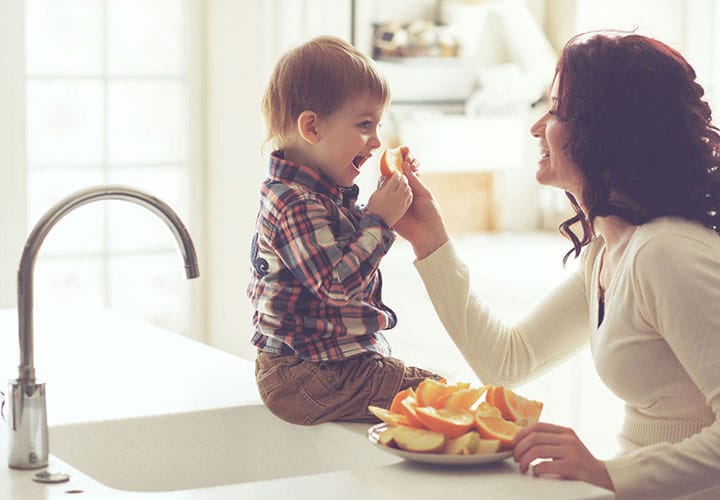 a mom feeding child oranges in the kitchen
