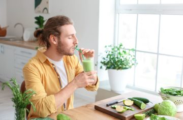 a man at his kitchen table taking a sip of a green smoothie