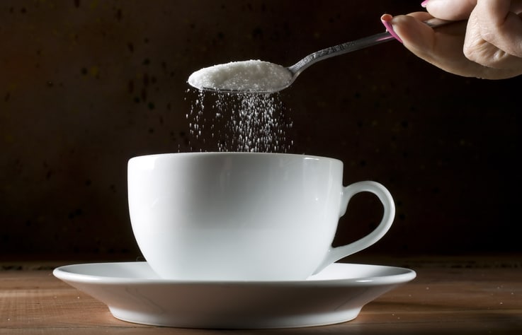 a woman adding sugar to a cup of tea
